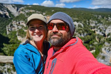 Orta yaşlı bir çift doğa yolunda yürürken selfie çekiyor.