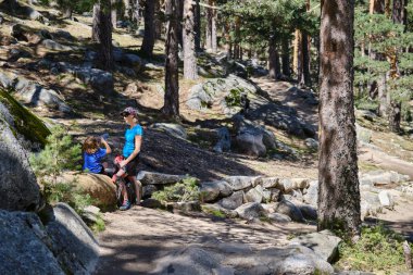Anne ve çocuk ormanda yürürken su içiyorlar.