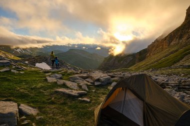 Anne ve oğul Pireneler 'deki çadırlarıyla dağda gün batımını izliyorlar.