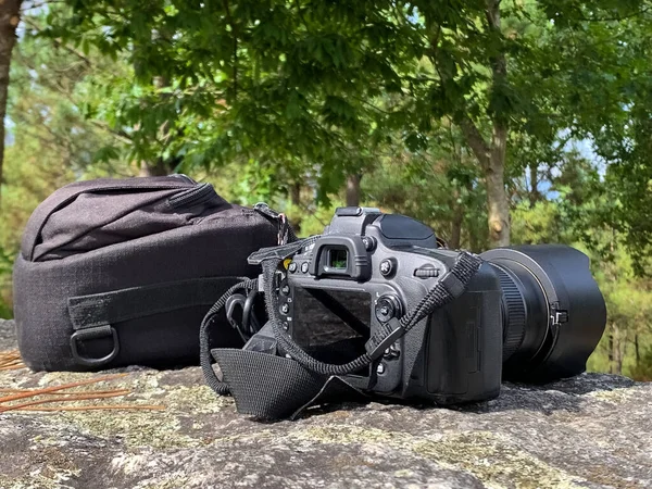 reflex camera with a bag on a stone against the background of green trees, the concept of travel photography