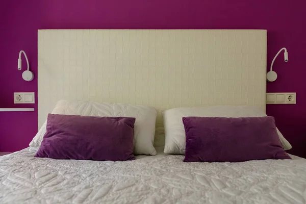 double bed with pillows and a white headrest against a lilac wall, close-up, modern bedroom interior
