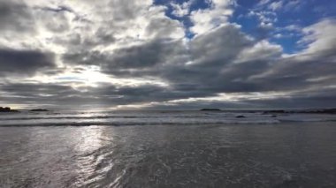 Dalgalar kumlu bir plaja yuvarlanıyor mavi gökyüzünün arka planında dramatik gök gürültülü bulutlar, gün batımı, güzel manzara, 4k ağır çekim