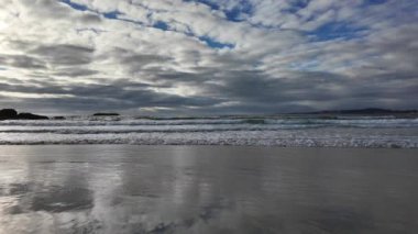 Dalgalar kumlu bir plaja yuvarlanıyor mavi gökyüzünün arka planında dramatik gök gürültülü bulutlar, gün batımı, güzel manzara, 4k ağır çekim