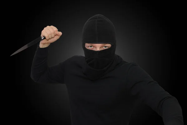 man in balaclava threatens with knife on a black background