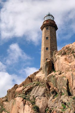 Bir kayanın üzerindeki deniz feneri, bulutlu mavi gökyüzünün arka planına karşı