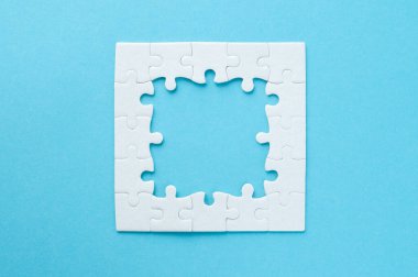 Yapbozun üst görüntüsü. Mavi arkaplanda bir çerçeve olarak beyaz kare yapboz.