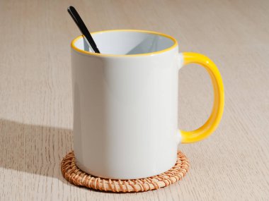 Sarı saplı ve iç kısımlı kupa. Çay kaşıklı kupa. Masadaki bardak altlığında iki tonluk bir bardak..