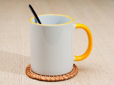 Sarı saplı ve iç kısımlı kupa. Çay kaşıklı kupa. Masadaki bardak altlığında iki tonluk bir bardak..