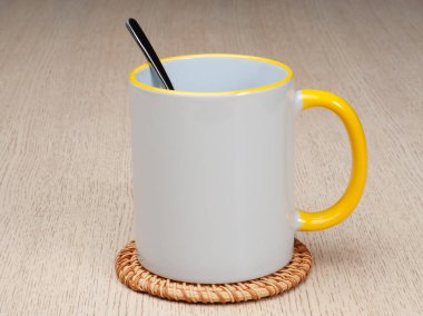 Sarı saplı ve iç kısımlı kupa. Çay kaşıklı kupa. Masadaki bardak altlığında iki tonluk bir bardak..