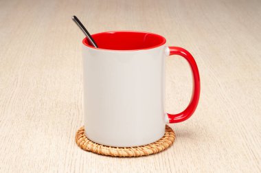 Kırmızı saplı ve iç kısımlı kupa. Çay kaşıklı kupa. Masadaki bardak altlığında iki tonluk bir bardak..