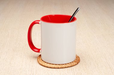 Kırmızı saplı ve iç kısımlı kupa. Çay kaşıklı kupa. Masadaki bardak altlığında iki tonluk bir bardak..