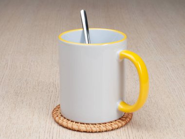 Sarı saplı ve iç kısımlı kupa. Çay kaşıklı kupa. Masadaki bardak altlığında iki tonluk bir bardak..