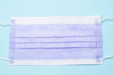 Mavi arka planda mor tıbbi maskenin üst görüntüsü. Sağlık, güvenlik, koruma ve tıbbi tasarım, stok resimleri ve sağlıkla ilgili projeler için ideal.