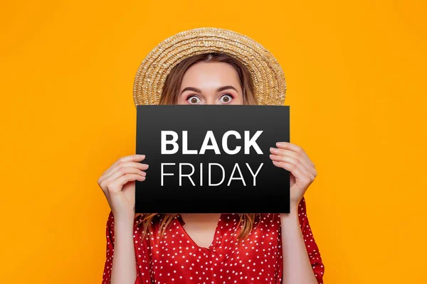 stock image shocked caucasian woman holding paper poster with black friday isolated on an orange studio background