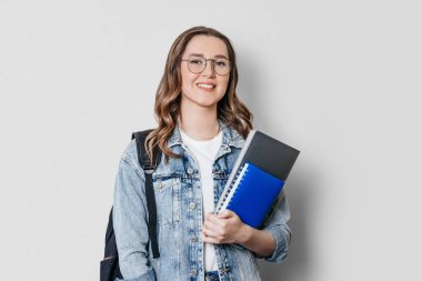 Sırt çantası gülüşlü öğrenci kız elinde defter, defter, klasör, koyu beyaz arka planda izole edilmiş ellerde. Eğitim, eğitim, sınavlar, İngilizce öğrenme kavramı.