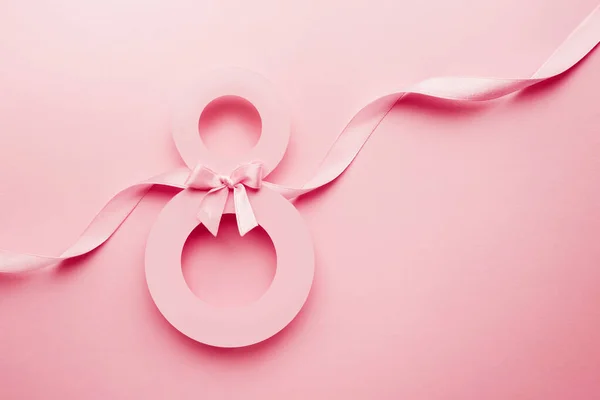 March 8 pink greeting card. Paper number 8 on a pink background with a ribbon and a bow, top view. copy space