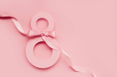 March 8 greeting card. Paper number 8 on a pink background with a ribbon and a bow, top view. copy space