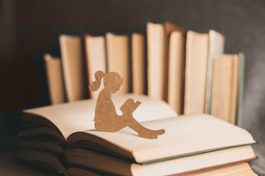 Küçük bir kız eski kitapların arka planında bir rüya kitabı okuyor. Elinde kitap olan bir kızın kağıt silueti. dünya bilgi günü konsepti