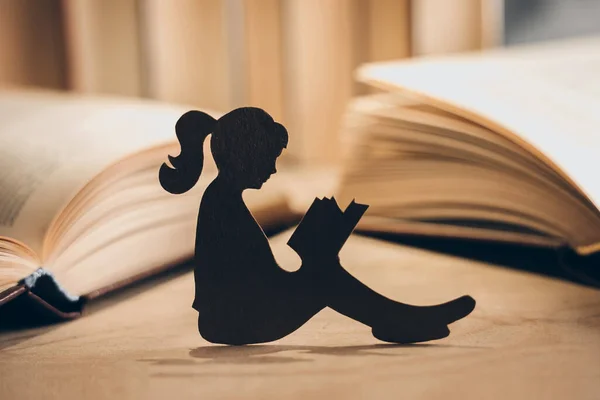 Silhouette of a girl reading a book in the library. paper figurine of a little girl sits among books and reads poetry. Introvert concept. Child psychology