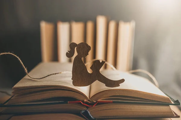 An introvert girl reads a bedtime story against the backdrop of books. Silhouette of a little girl sitting in a library of books. World Knowledge Day. Book Day. Child psychology