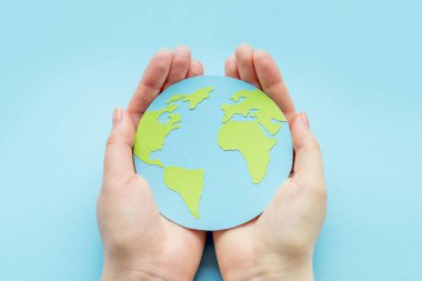 Dünya çevre günü konsepti. İki insan eli, mavi arka planda dünyadan izole edilmiş kağıt küreyi tutuyor. Dünya günü
