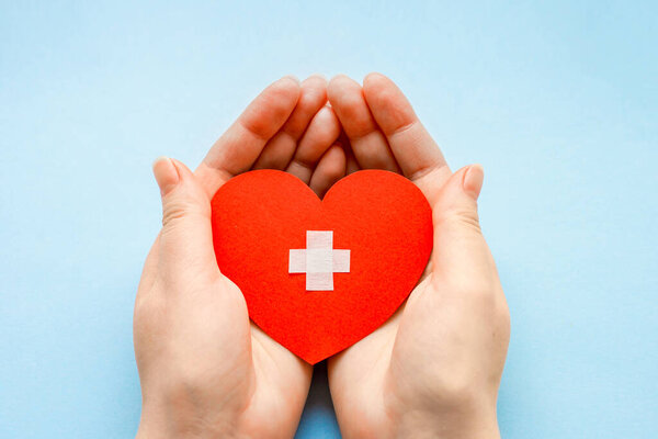 Всемирный день здоровья. люди и кардиологическая концепция. Закрытие женских рук с медицинским крестом на маленьком красном бумажном сердце