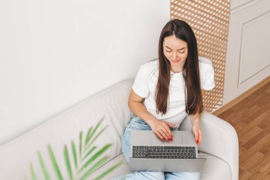 Kız evde dizüstü bilgisayarda çalışıyor, kanepede oturuyor ve iş için boş yer arıyor.