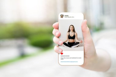 Güzel mankenin fotoğrafına bakan bir kadın cep telefonunda yoga yapıyor. Kadın eli akıllı olanı tutuyor ve sosyal medyada geziniyor.