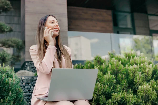 stock image Portrait of business woman working outside. Smiling corporate woman with laptop, making phone call and sitting near office building