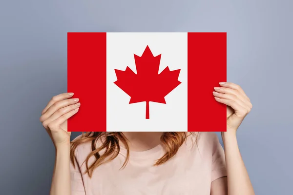 female hands holds blank white speech bubble with canadian flag isolated on blue background. Invitation to study in Canada concept
