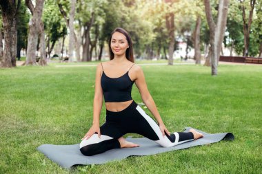 Genç esmer, beyaz kadın parkta egzersiz yaparken yoga yapıyor. Sağlıklı bir yaşam tarzı. Doğada fiziksel egzersiz.