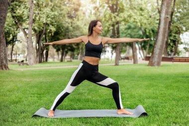 Yoga minderinde duran, yoga yapan, parkta pilates yapan genç bir kadın. sağlıklı yaşam tarzı kavramı