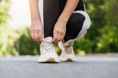 Genç bir kadının spor ayakkabılarını bağlarken dışarıda koşuya hazırlanmasına yakın çekim. Sağlık ve spor konsepti