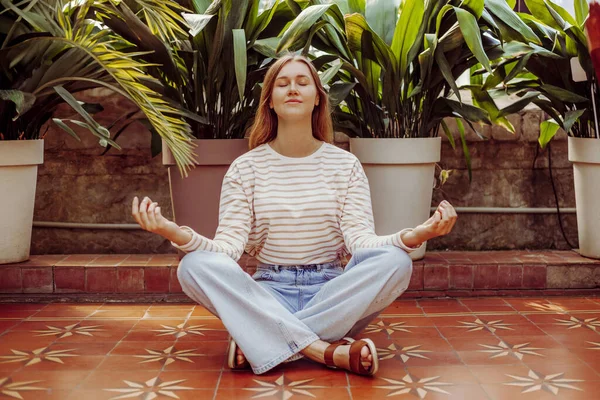 Woman practicing yoga and meditation sitting in lotus pose on the background of a tropic leaves. Mindful meditation concept. Wellbeing.