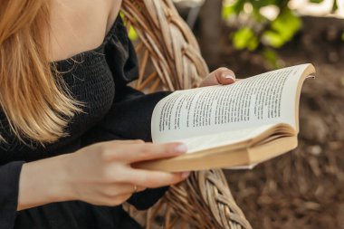 Klasik bir kitap tutan kadın elleri. Kapat. Kız saman sandalyede oturmuş kitap okuyor.