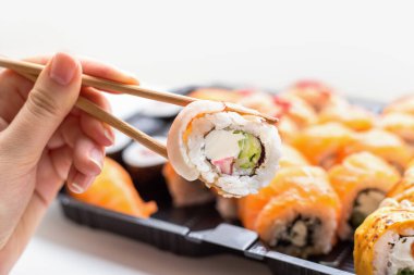 Bambu çubukları ve kadın eli olan beyaz bir zemin üzerinde suşi ruloları.