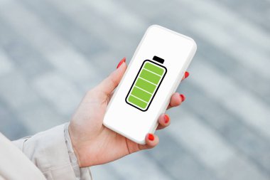 Cep telefonuna tam şarj. Sokakta arka planda tam şarjlı bir akıllı telefonu tutan bir kadın.