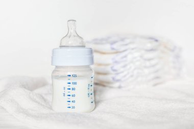 Beyaz kumaş arka planında süt ve bebek bezi olan bebek şişesi. Bebek bakımı. Hayatın ilk günleri. Beslenme ve annelik