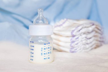 Beyaz kumaş arka planında süt ve bebek bezi olan bebek şişesi. Bebek bakımı. Hayatın ilk günleri. Beslenme ve annelik
