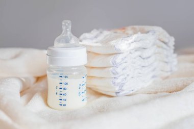 Beyaz kumaş arka planında süt ve bebek bezi olan bebek şişesi. Bebek bakımı. Hayatın ilk günleri. Beslenme ve annelik