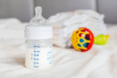 Beyaz kumaş arka planında süt ve bebek bezi olan bebek şişesi. Bebek bakımı. Hayatın ilk günleri. Beslenme ve annelik