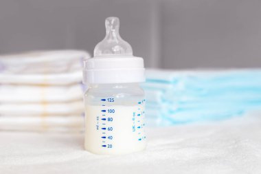 Beyaz kumaş arka planında süt ve bebek bezi olan bebek şişesi. Bebek bakımı. Hayatın ilk günleri. Beslenme ve annelik. Tek kullanımlık nem emme bezi.