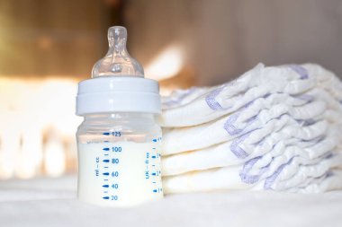 Beyaz kumaş arka planında süt ve bebek bezi olan bebek şişesi. Bebek bakımı. Hayatın ilk günleri. Beslenme ve annelik
