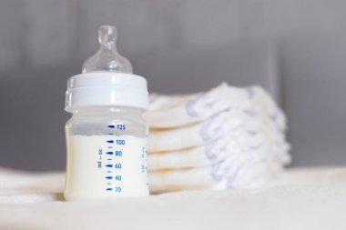 Beyaz kumaş arka planında süt ve bebek bezi olan bebek şişesi. Bebek bakımı. Hayatın ilk günleri. Beslenme ve annelik