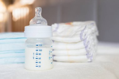 Beyaz kumaş arka planında süt ve bebek bezi olan bebek şişesi. Bebek bakımı. Hayatın ilk günleri. Beslenme ve annelik. Tek kullanımlık nem emme bezi.