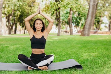 Genç esmer, beyaz kadın parkta egzersiz yaparken yoga yapıyor. Sağlıklı bir yaşam tarzı. Doğada fiziksel egzersiz. Kız parkta meditasyon yapıyor.