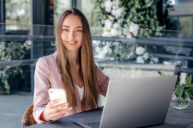 Bir kafeden uzaktan çalışan, dizüstü bilgisayar kullanan, gülümseyen, kameraya bakan genç bir kadın. Pazarlamacı, Analist