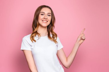 Mutlu öğrenci kız gülümser ve boş fotokopi alanını gösterir, kapat. Pembe arka planda izole edilmiş genç bir kadının portresi.