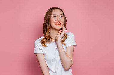 Beyaz tişörtlü, beyaz tenli, beyaz tenli, esmer kadın. Stüdyoda pembe arka planda izole bir şekilde gülümsüyor ve başka tarafa bakıyordu. Boşluğu kopyala