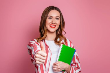 Öğrenci kız elinde bir egzersiz kitabı tutuyor ve el hareketleriyle pembe arkaplanı izole ediyor. Boşluğu kopyala.